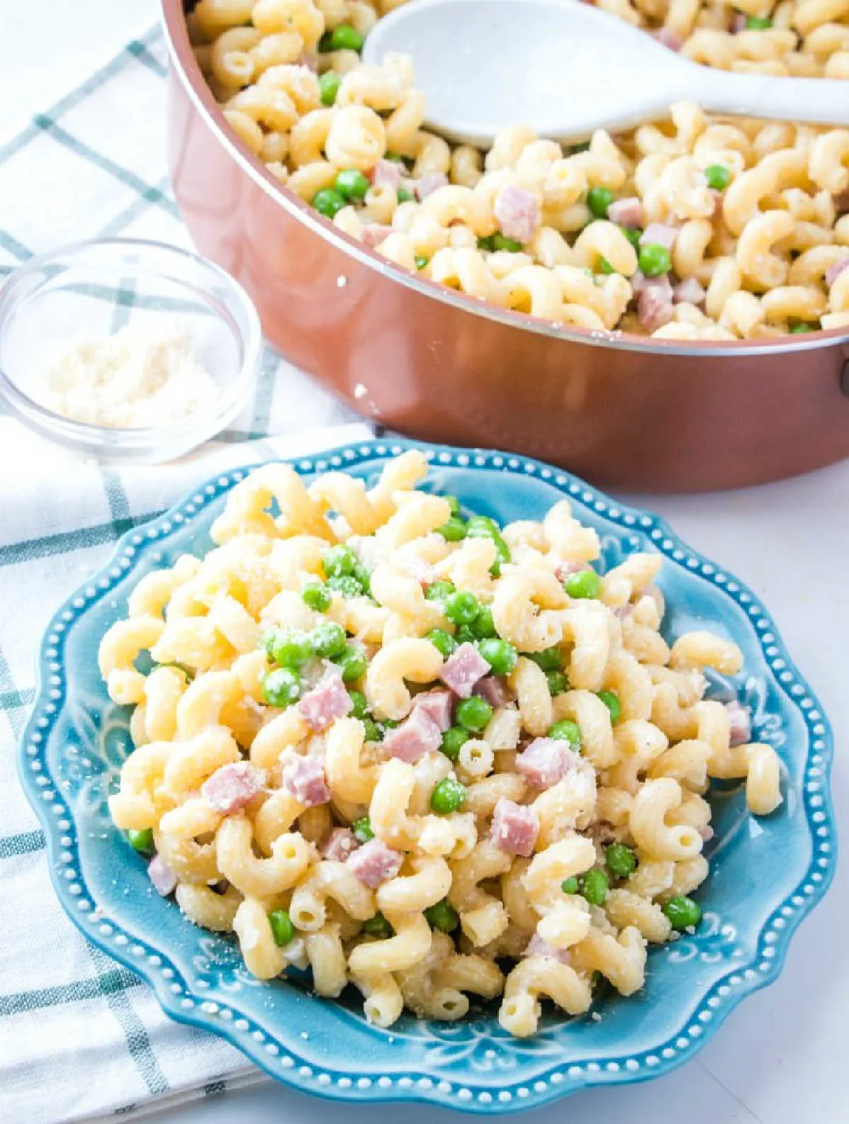 plate of served pasta with ham and peas in front of pan of remaining pasta.