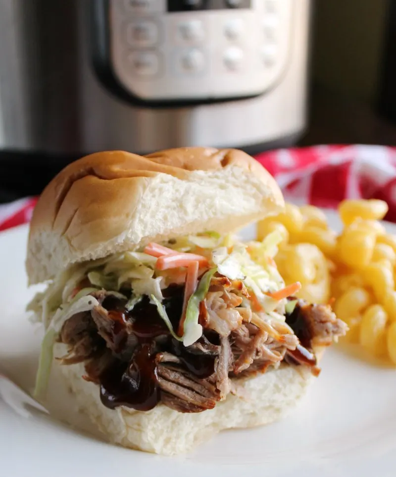 pulled pork on bun with macaroni and cheese and instant pot in background.