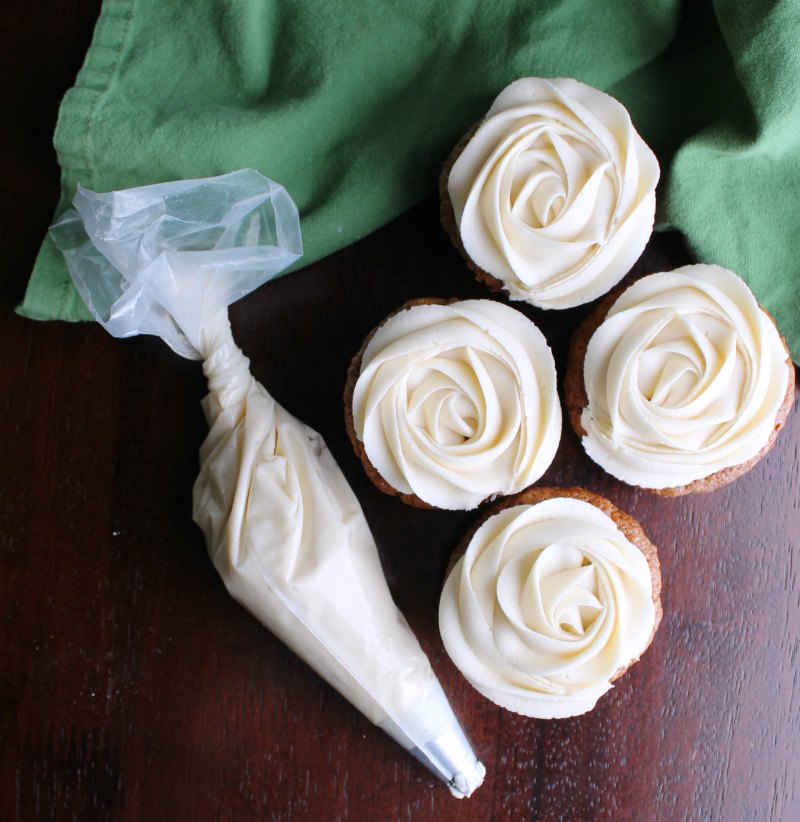 rosettes of caramel buttercream on carrot cupcakes next to piping bag of more frosting.