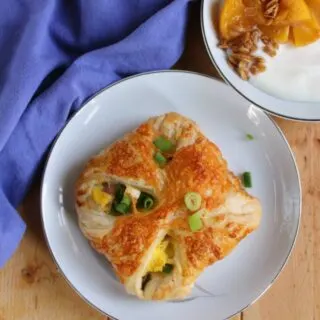 ham egg and cheese hand pie with scallions on top and a bowl of yogurt with peaches and granola in the background.
