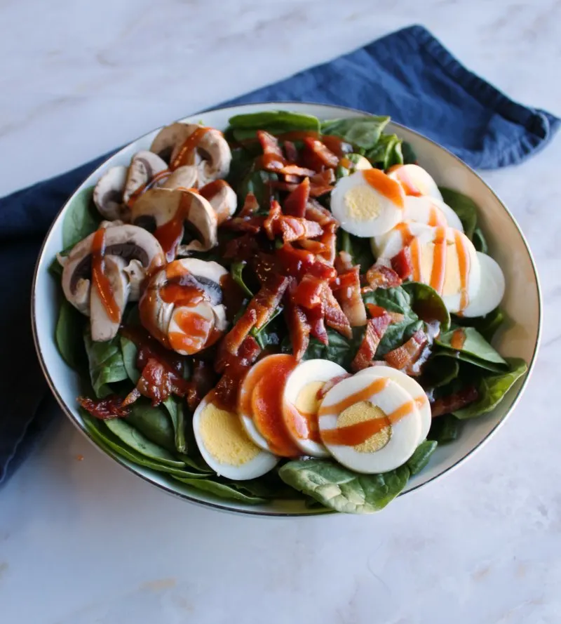 Close up bowl of spinach salad with red dressing drizzled over the top.
