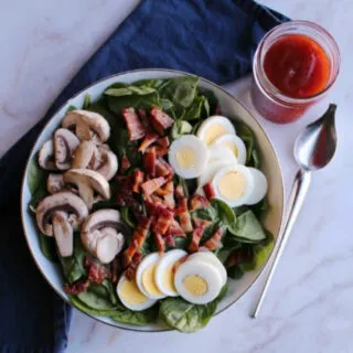 bowl of spinach salad with eggs, bacon, mushrooms and homemade dressing.