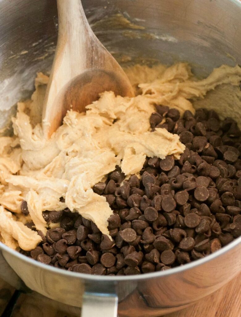 mixer bowl full of brown sugar dough and lots of chocolate chips with wooden spoon.