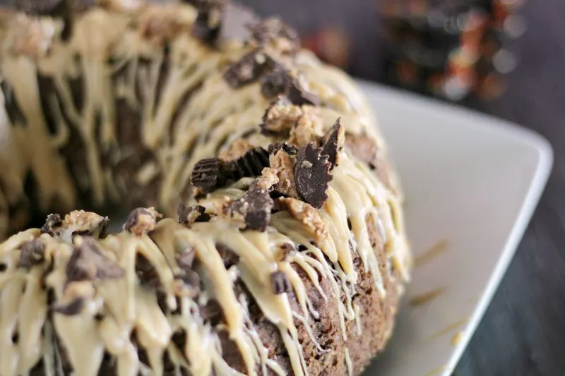 close up of top of chocolate bundt cake with peanut butter drizzle and chopped peanut butter cups on top.