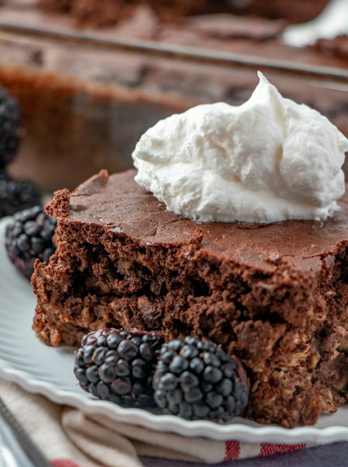 close up of brownie baked oatmeal slice with blackberries and whipped cream