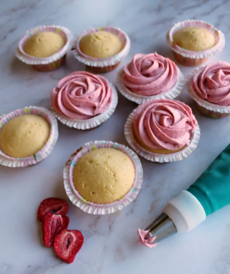 vanilla cupcakes getting strawberry buttercream piped on.