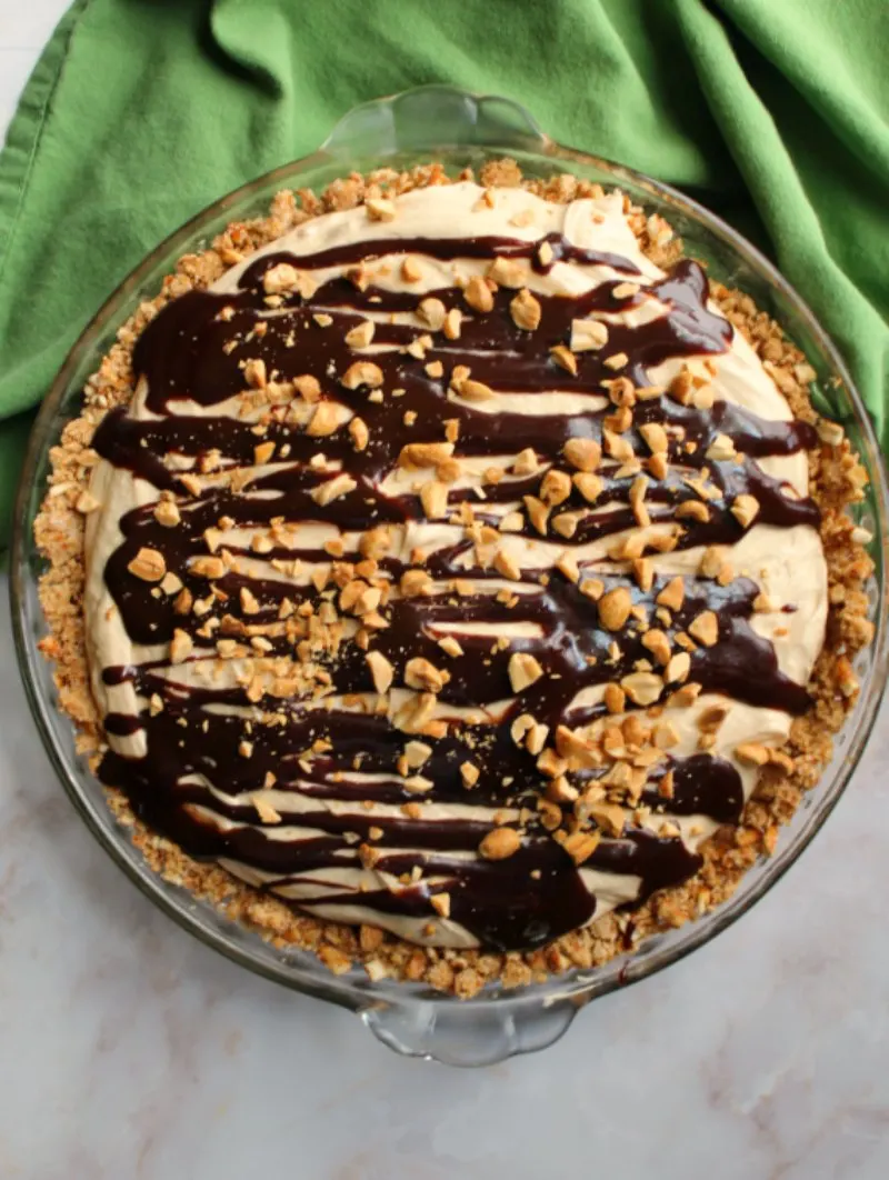 fluffy peanut butter pie with pretzel crust, fudge drizzle and chopped peanuts on top.