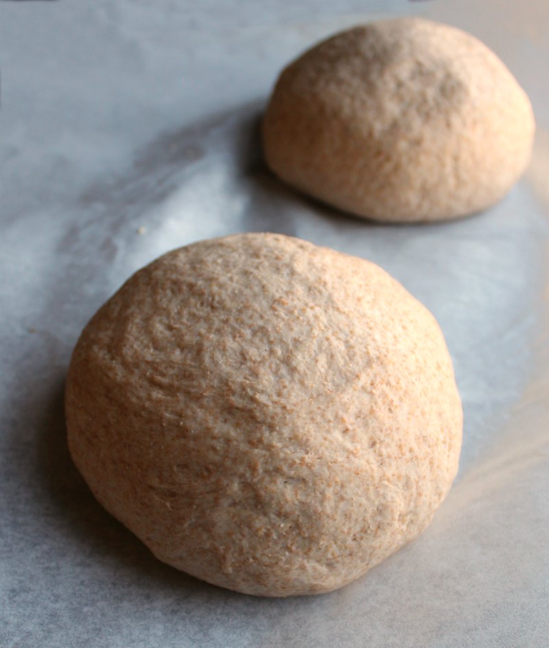 two balls of whole wheat pizza dough on parchment paper