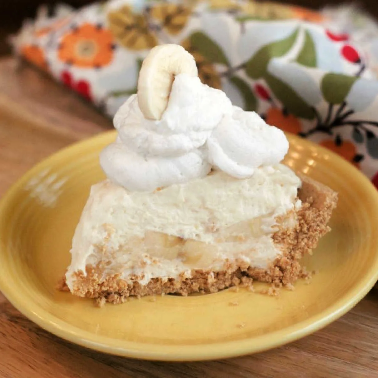 Slice of no cook banana cream pie with a pile of whipped cream on top on a yellow plate.