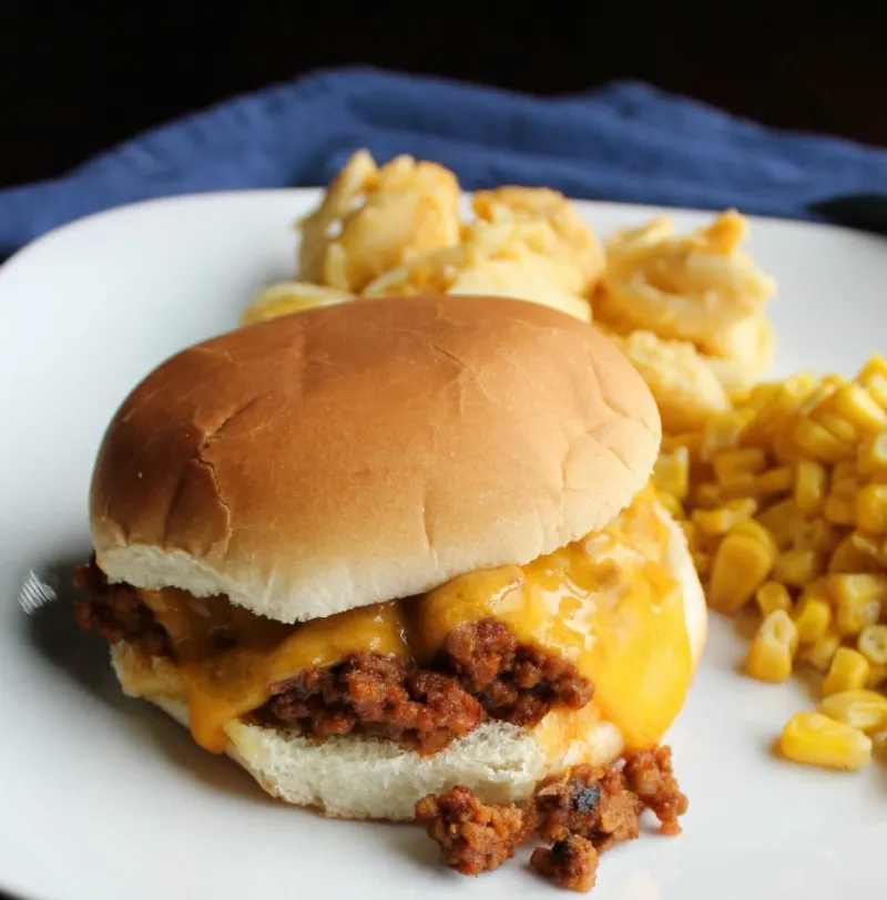 sloppy joe sandwich with melted cheddar cheese on it, macaroni and cheese and corn in the background.