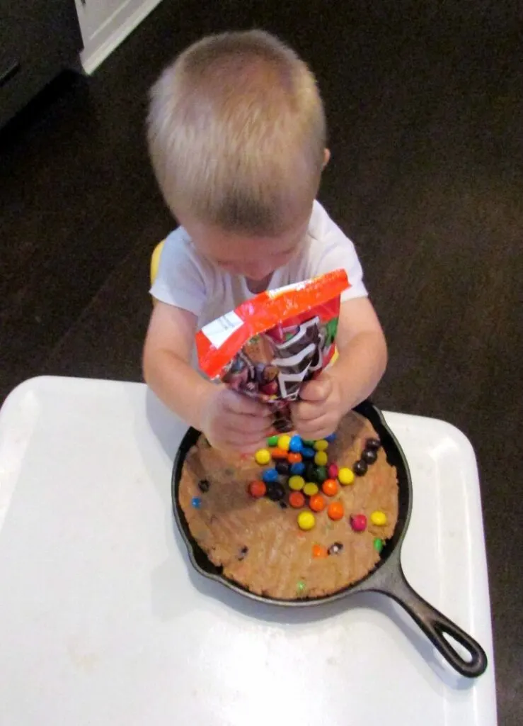 Little dude pouring extra m&ms on top of skillet cookie.
