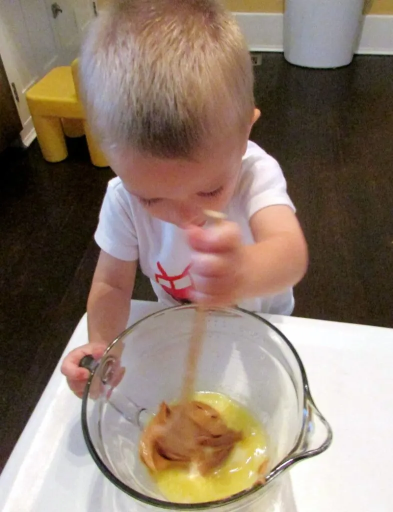 little dude stirring melted butter and peanut butter in a glass mixing bowl.