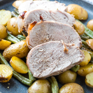 Slices of pork tenderloin served on top of potatoes and green beans.