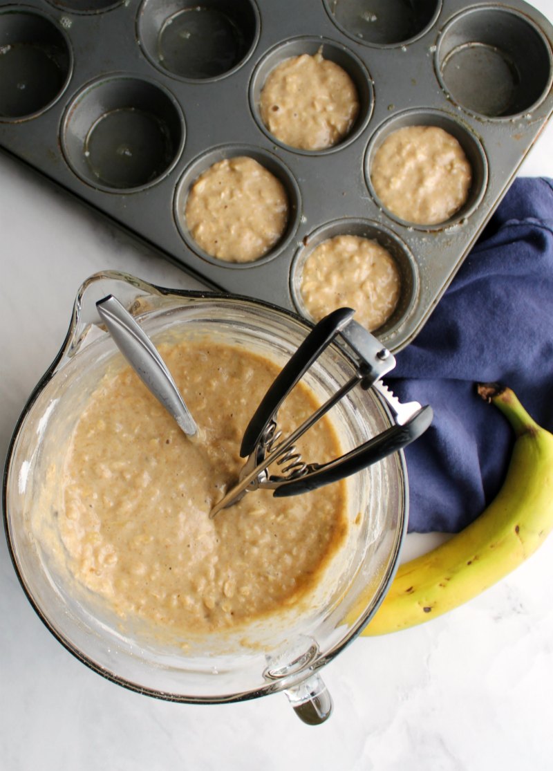 bowl of banana oat muffin batter with cookie scoop and cupcake pan with batter in it almost ready to bake.