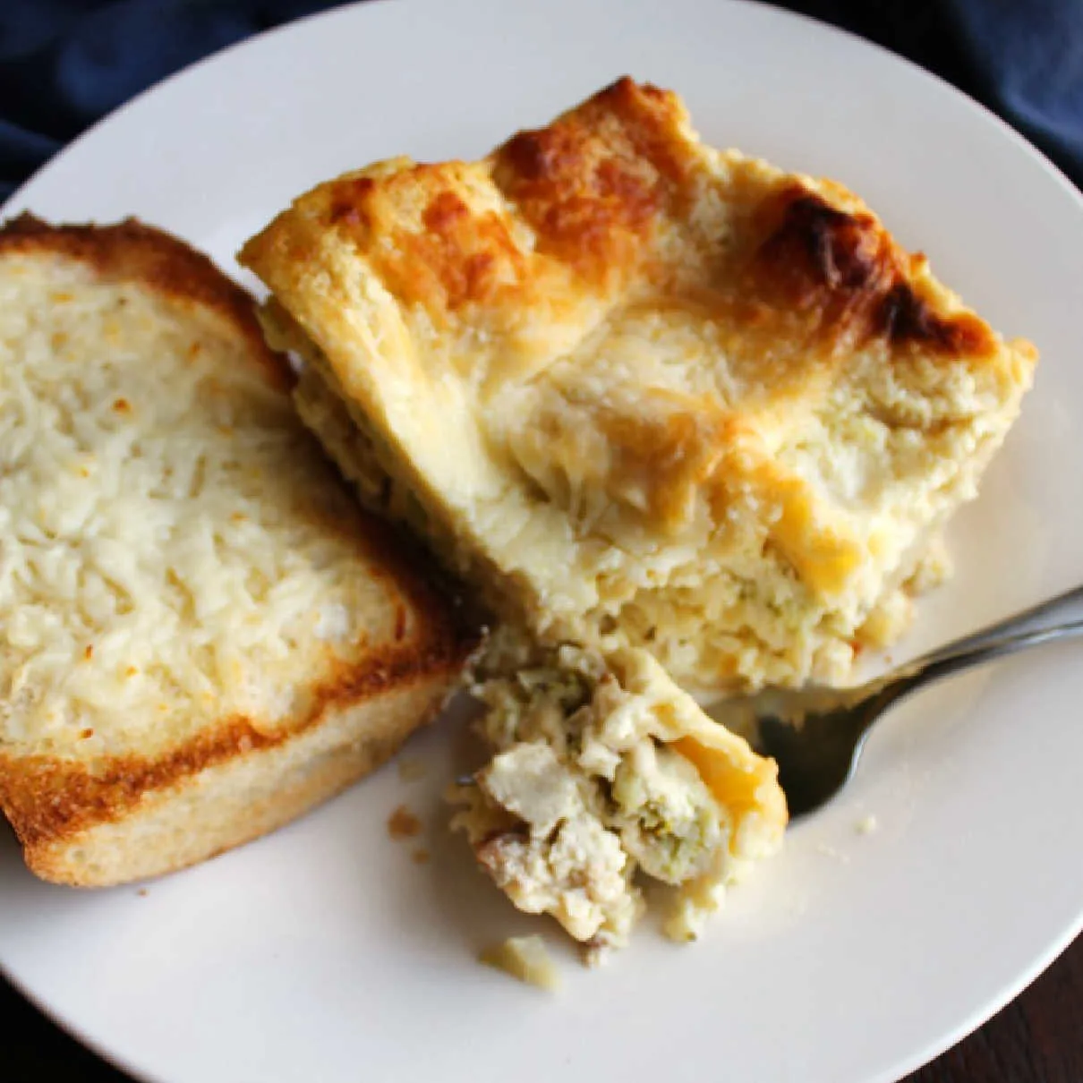 plate with white chicken and broccoli lasagna and piece of garlic bread.