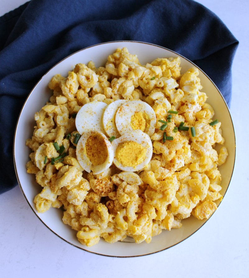 serving bowl full of deviled egg macaroni salad with sliced hard boiled eggs, paprika and chives on top.