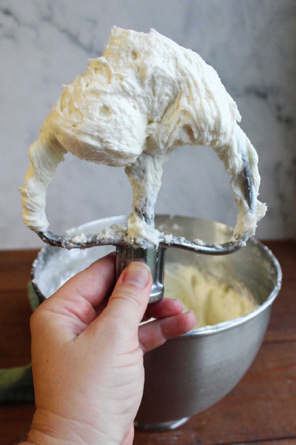 Hand holding mixer paddle with a bunch of fluffy decorator's cream cheese frosting on it, ready to be used.