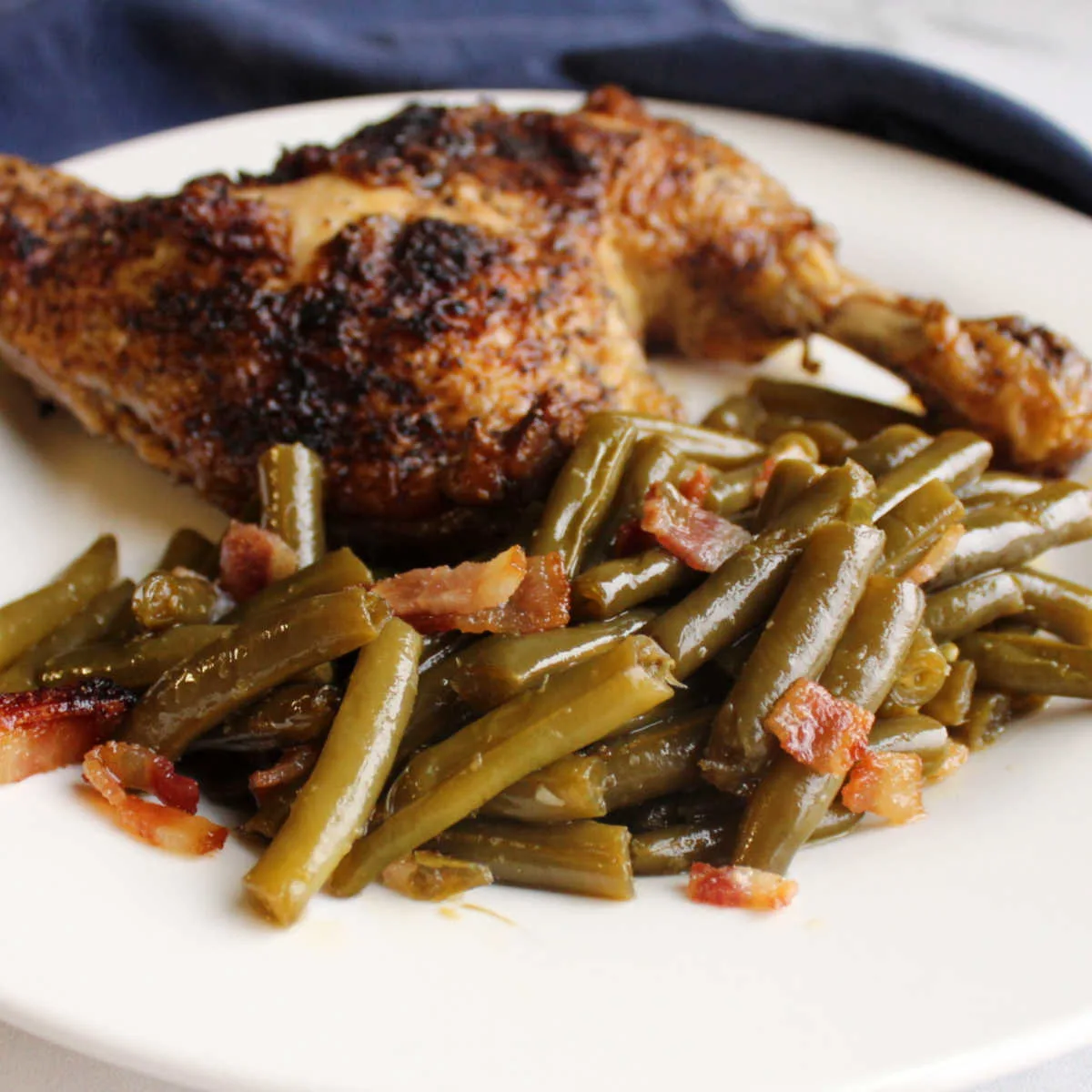 Smothered green beans with bacon and sweet and sour sauce served with grilled chicken on a plate.