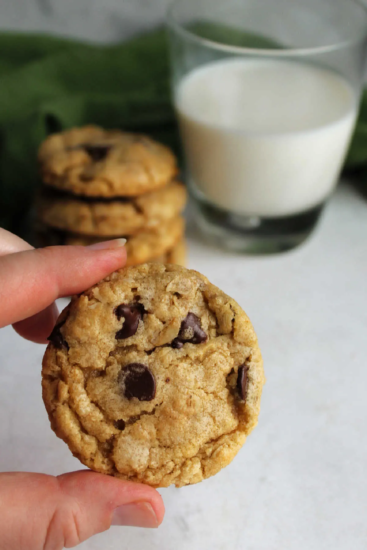 Hand holding a fresh baked cowgirl cookie with bits of oats and chocolate chips showing. 