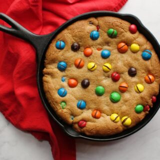Cast iron skillet filled with peanut butter cookie with M&Ms on top.