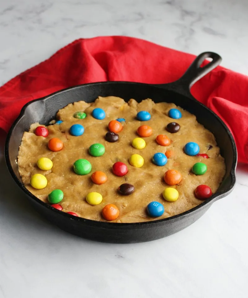 Peanut butter cookie dough pressed into cast iron skillet with peanut butter m&ms on top.