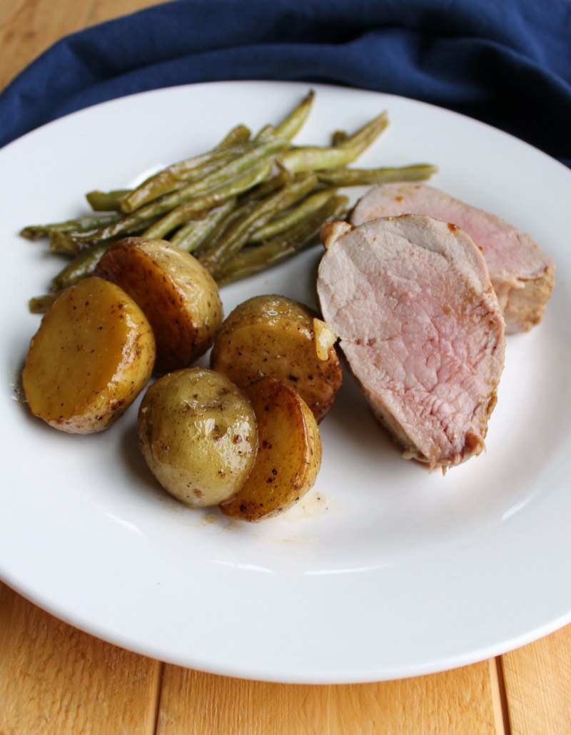 pork tenderloin dinner served on plate with roasted potatoes and green beans. 