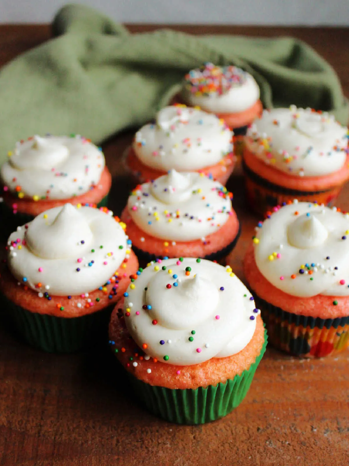 Smooth swirls of decorator's cream cheese frosting piped on pink strawberry cupcakes and topped with colorful sprinkles.