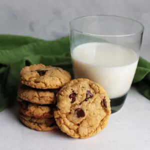 Stack of freshly baked brown butter cowgirl cookies with chocolate chips and oatmeal next to cup of milk.