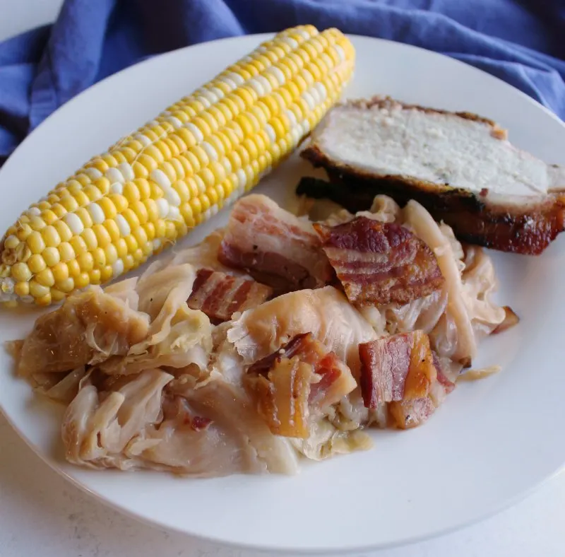 dinner plate with cabbage, corn on the cob and bacon wrapped pork loin