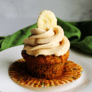 Banana cupcake with swirl of banana buttercream on top with a slice of banana on top.