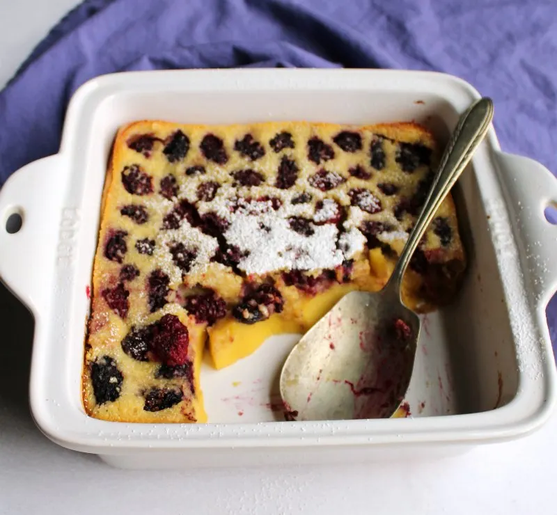 Vintage berry spoon in pan with custardy clafoutis dotted with blackberries.