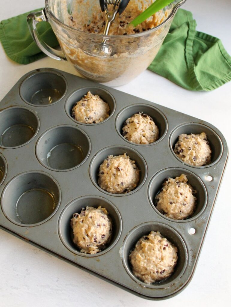scooping chocolate chip oatmeal sourdough batter into muffin tin.