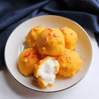 Bowl of small orange chocolate coated balls of ice cream with sprinkles, one cut open to show creamy vanilla ice cream center.