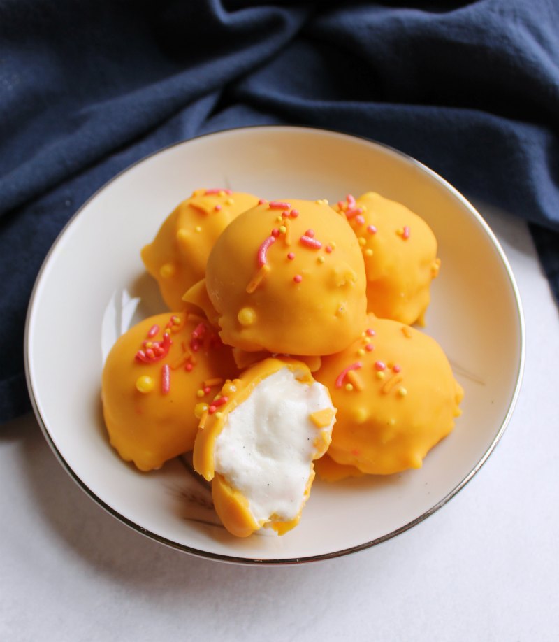 bowl full of orange ice cream bon bons covered with orange, pink and yellow sprinkles. One opened to see white ice cream inside. 