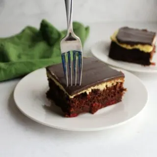 Fork piercing through ganache on top of vanilla buttercream coated chocolate and cherry black forest cake.