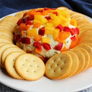 Havarti cheese ball with pieces of colorful sweet peppers on the outside with crackers, ready to eat.