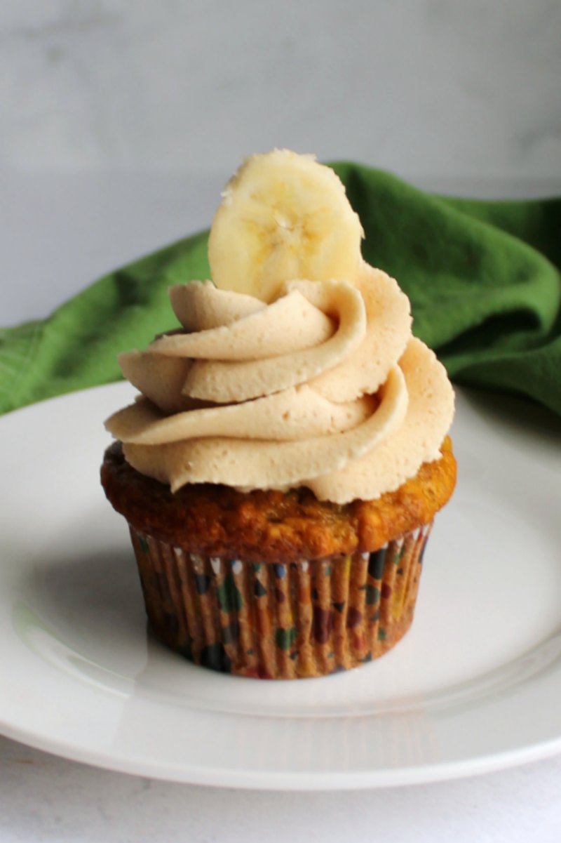 banana cupcake with swirl of fluffy peanut butter and brown sugar buttercream and a slice of banana on top.