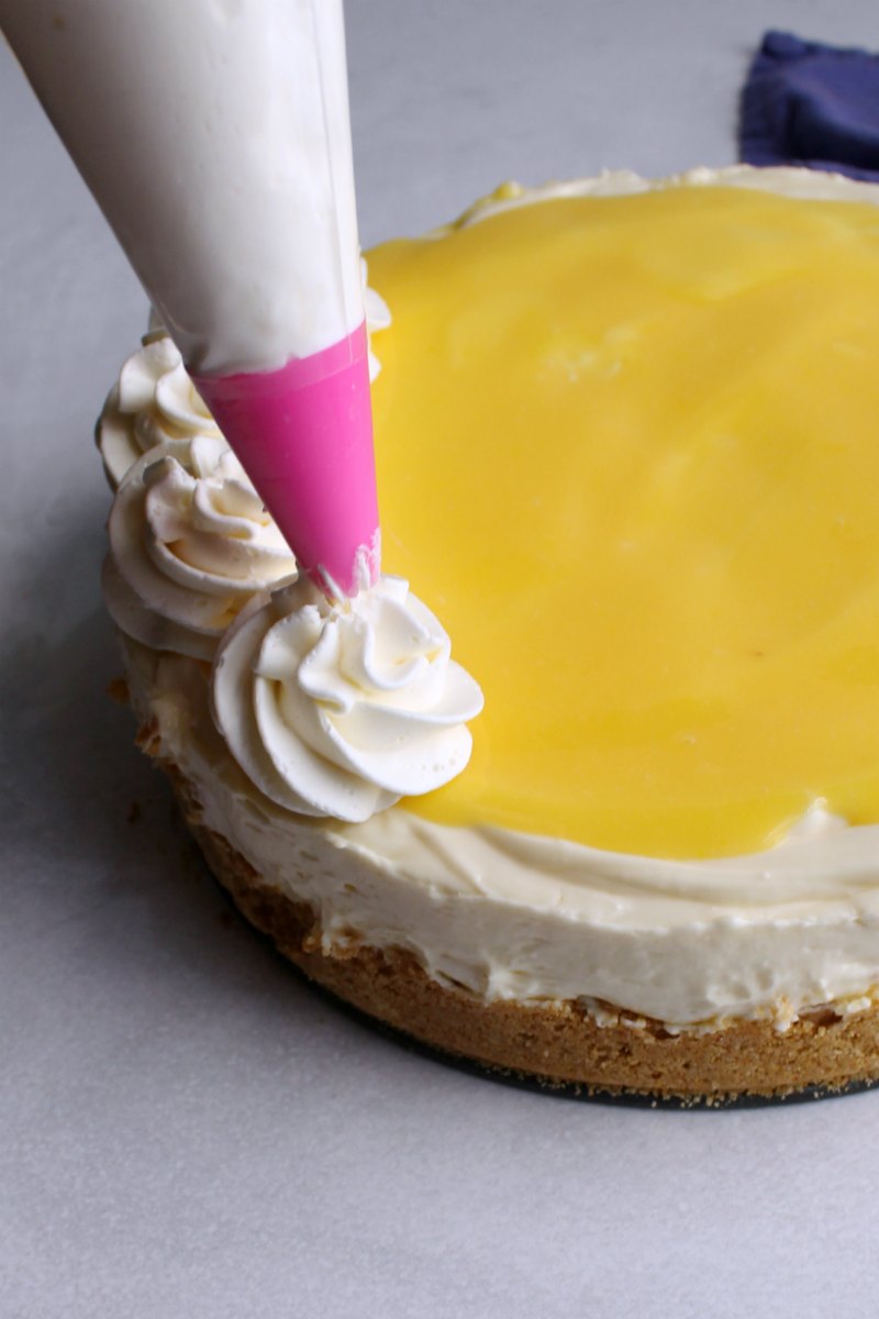 piping swirls of cream cheese whipped cream on top of lemon curd topped no bake cheesecake.