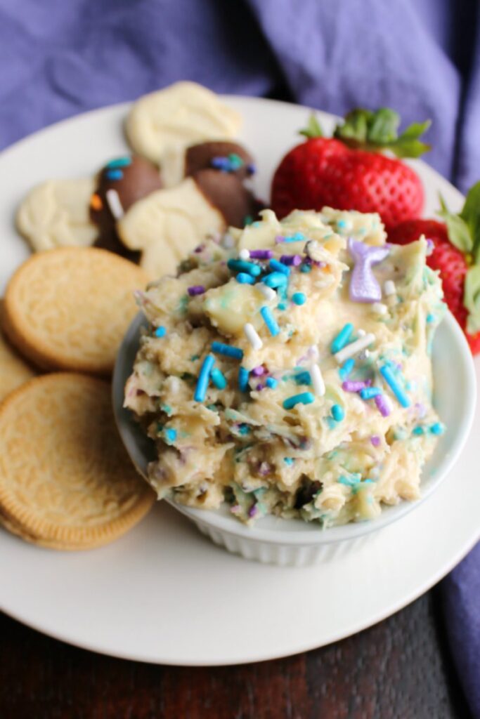 ramekin of birthday cookie dough dip with extra sprinkles on top on small plate with berries, animal crackers and oreo dippers.