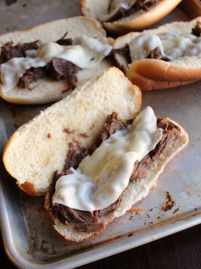 baking tray with toasted rolls pile with shredded Italian beef and melted provolone.