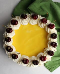 lemon no bake cheesecake topped with whipped cream swirls and fresh cherries.