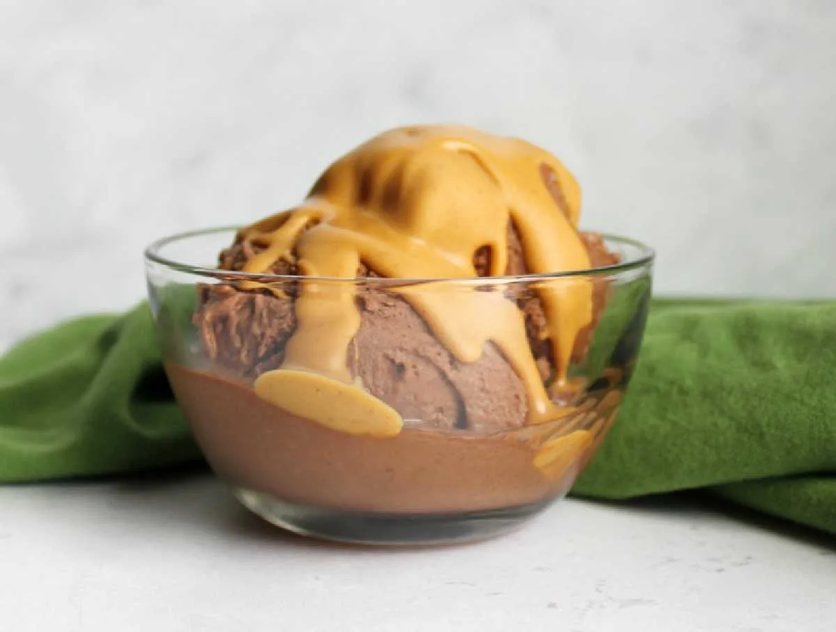 glass bowl of chocolate and peanut butter nice cream scoops with peanut butter magic shell on top.