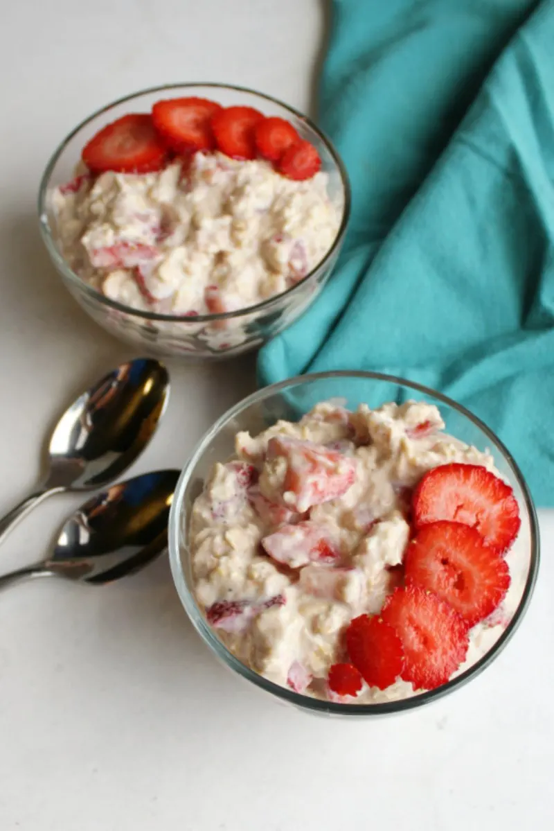 looking down at two bowls of strawberries and cream overnight oats with fresh strawberry sliced on top.