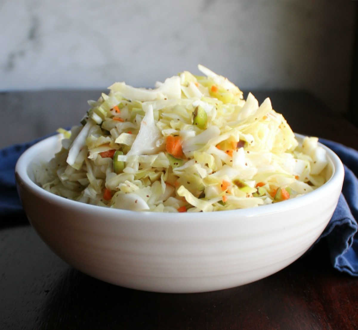 close up of a white serving bowl loaded with tangy vinegar based coleslaw.