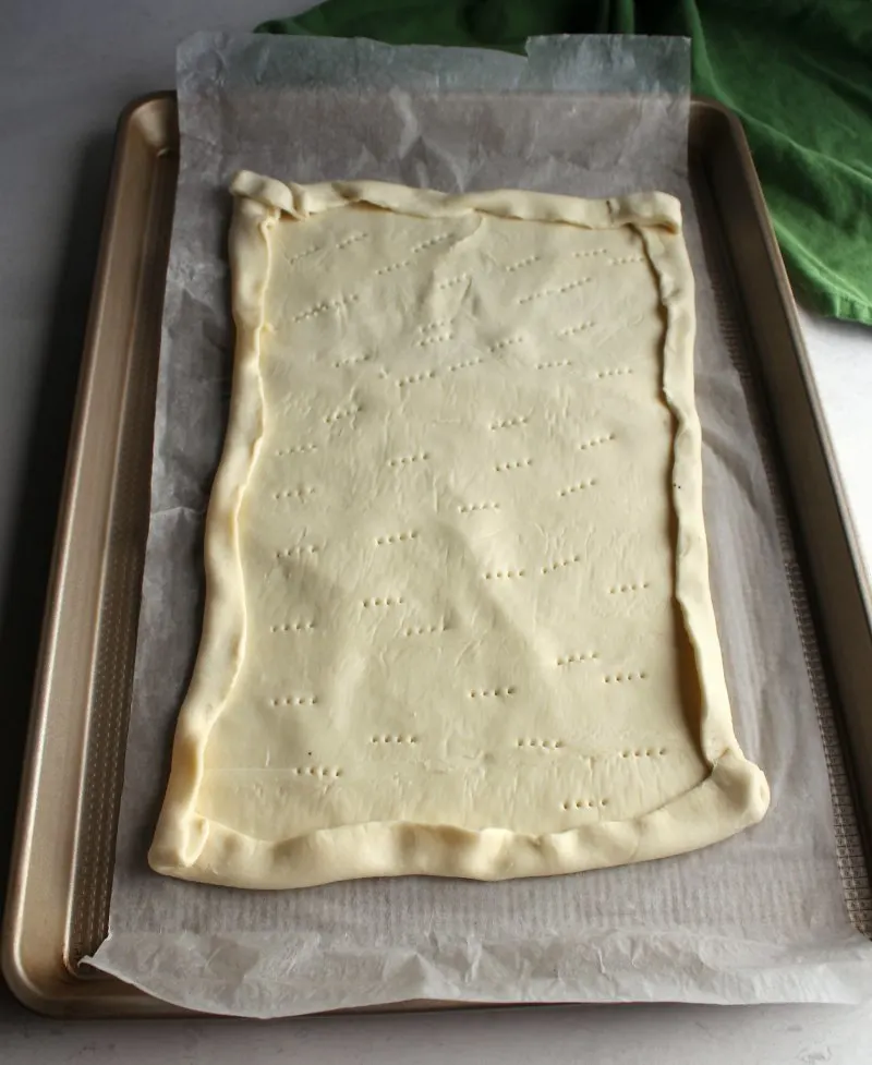 puff pastry dough sheet with edges folded over and docked center ready to bake.