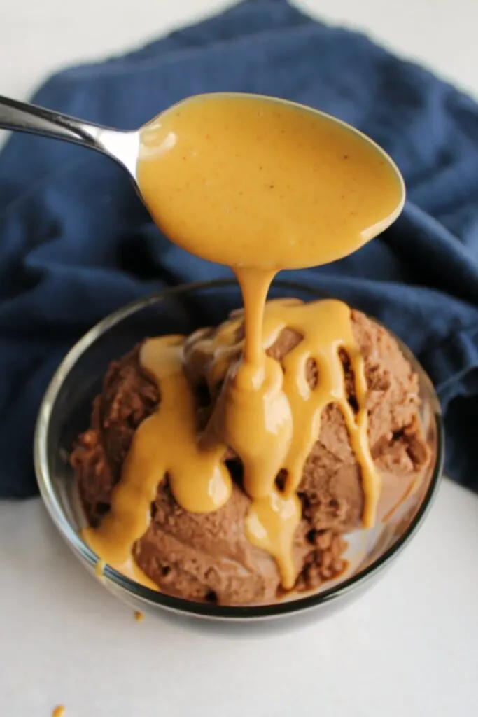 spoon drizzling peanut butter magic shell over bowl of chocolate nice cream.