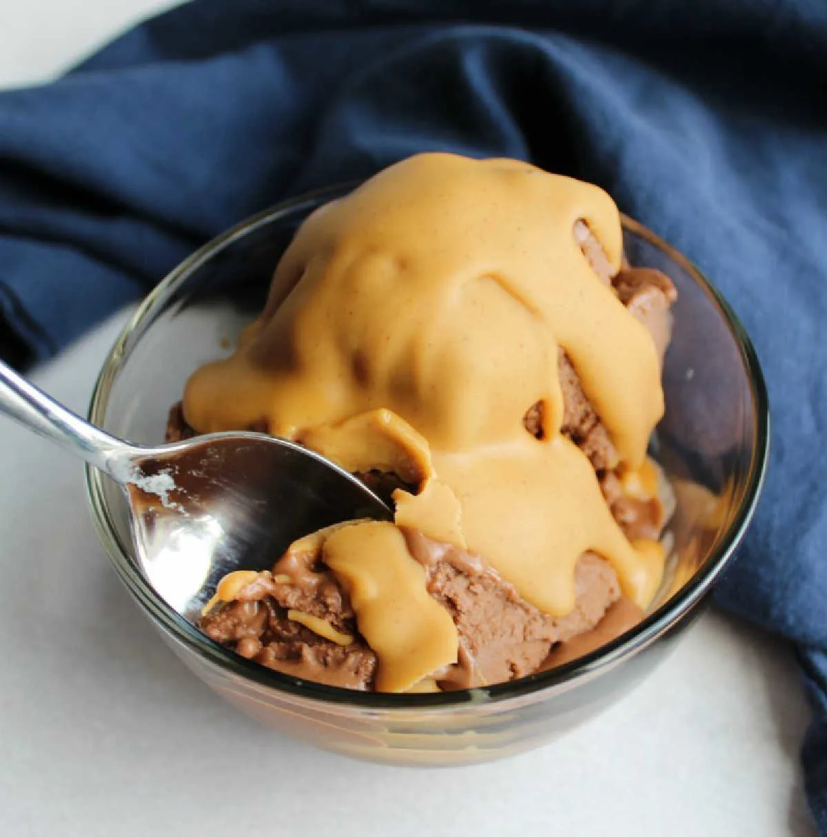 bowl of chocolate peanut butter banana ice cream with peanut butter magic shell on top with blue napkin.