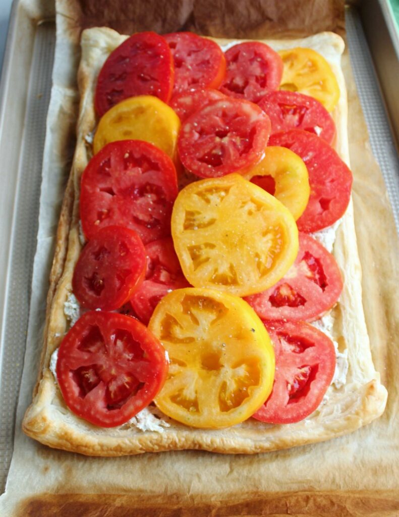 layers of fresh yellow and red tomatoes on top of ricotta and puff pastry ready to bake.