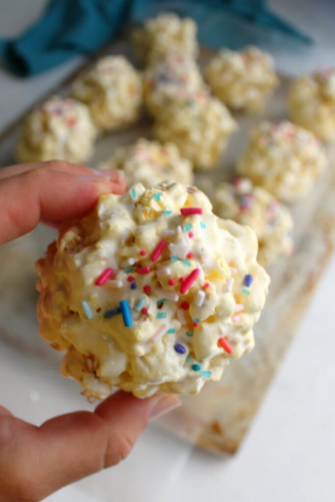 hand holding a sprinkle topped marshmallow popcorn ball with remaining popcorn balls in the background.