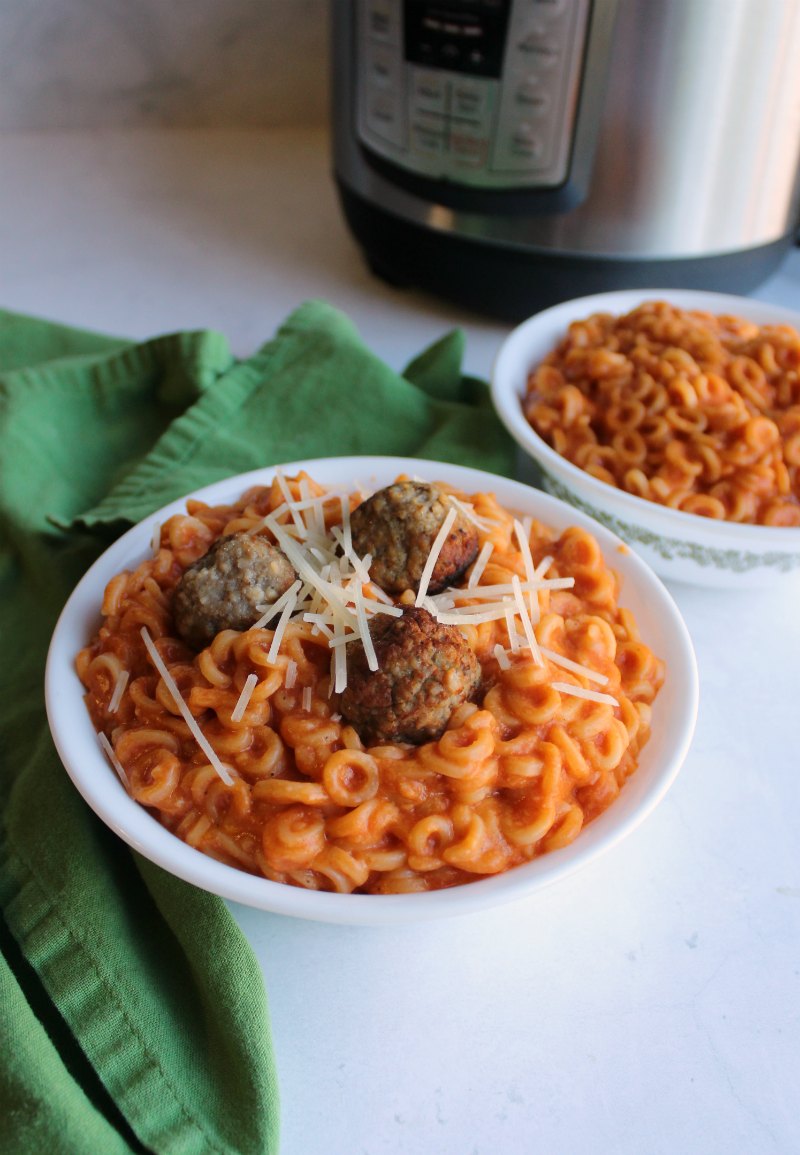 bowl of homemade copycat spaghettios with meatballs and shreds of Parmesan cheese in front of pressure cooker.